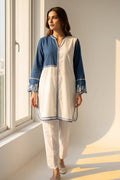 Woman wearing a blue and white traditional outfit standing by a window with sunlight streaming in.